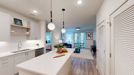 Located at 222 N West St in the heart of downtown Raleigh, NC, this thoughtfully designed 2-bedroom, 2-bathroom residence offers a clean, contemporary aesthetic throughout. The open-concept living area seamlessly connects the kitchen, dining, and living spaces, all finished with warm wood-look flooring and crisp white walls. The modern kitchen is a standout feature, boasting a large center island with quartz countertops, white cabinetry, stainless steel appliances, and globe pendant lighting that adds a stylish focal point. The living and dining area is bathed in natural light from full-length windows and a glass door leading to a private balcony. Both bedrooms are well-appointed, featuring ceiling fans, large windows, and generous closet space. The primary suite includes a spacious walk-in closet with custom built-in shelving and drawers. The en-suite bathroom offers a dual-sink vanity with a backlit mirror and a glass-enclosed tile shower. The second bathroom mirrors the same refined finishes. Additional highlights include multiple closets, a dedicated laundry area, and a utility room, ensuring ample storage throughout. The overall ambiance is light, airy, and move-in ready.