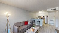 Located at 919 East Lemon Street in Tempe, Arizona, this one-bedroom, one-bathroom unit offers a well-designed single-floor layout that maximizes every inch of its compact footprint. The open-concept living and kitchen area serves as the heart of the home, where light wood-style vinyl flooring flows seamlessly throughout, complemented by a textured ceiling and painted concrete brick accent walls that lend a subtle industrial character to the space.

The kitchen is efficiently designed with crisp white cabinetry, a geometric tile backsplash, stainless steel appliances including a refrigerator and range, and a peninsula countertop with bar seating — ideal for casual dining. The living area benefits from natural light through a window near the entry, offering a bright and airy atmosphere.

The bedroom is a cozy, well-proportioned retreat featuring the same painted brick accent wall, a window that brings in natural light, and ample wall space for storage and furnishings. The full bathroom includes a tub and shower combination with sliding glass doors, a single vanity with a white countertop, and clean, neutral finishes throughout. Overall, this unit presents a modern, functional living environment in a prime Tempe location.