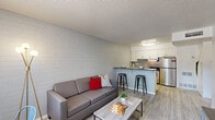 Located at 919 East Lemon Street in Tempe, Arizona, this one-bedroom, one-bathroom unit offers a well-designed single-floor layout that maximizes every inch of its compact footprint. The open-concept living and kitchen area serves as the heart of the home, where light wood-style vinyl flooring flows seamlessly throughout, complemented by a textured ceiling and painted concrete brick accent walls that lend a subtle industrial character to the space.

The kitchen is efficiently designed with crisp white cabinetry, a geometric tile backsplash, stainless steel appliances including a refrigerator and range, and a peninsula countertop with bar seating — ideal for casual dining. The living area benefits from natural light through a window near the entry, offering a bright and airy atmosphere.

The bedroom is a cozy, well-proportioned retreat featuring the same painted brick accent wall, a window that brings in natural light, and ample wall space for storage and furnishings. The full bathroom includes a tub and shower combination with sliding glass doors, a single vanity with a white countertop, and clean, neutral finishes throughout. Overall, this unit presents a modern, functional living environment in a prime Tempe location.