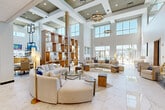 Located on Sunset Lake Drive in Shiloh, Illinois, this impressive single-floor clubhouse spans a generous footprint and showcases upscale design throughout. The centerpiece is a soaring, double-height living area adorned with polished marble-look tile flooring, dramatic floor-to-ceiling windows, and statement ring chandeliers that bathe the space in warm, ambient light. Curved, neutral-toned sofas are arranged around glass-topped coffee tables, creating an inviting social atmosphere, while a tall open-shelving unit displays decorative ceramics, adding an artistic focal point.

A full-service bar with warm wood cabinetry, a white quartz countertop, and an overhead wine glass rack anchors one wing of the space, complemented by high ceilings and views of the outdoor pool area. A dedicated dining zone features a mix of white-topped tables and pendant lighting, accented by vibrant large-scale artwork on the walls.

The lounge area includes a sleek, dark marble fireplace surround topped by a large multi-panel display screen, flanked by accent chairs for an intimate retreat. A reception desk near the entrance provides a welcoming arrival point. Throughout, the space benefits from generous natural light, lake views, and a cohesive modern aesthetic defined by gold accents, clean lines, and curated decor.