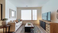 This thoughtfully designed single-floor residence combines modern aesthetics with functional living across a well-organized floor plan. The living room is bright and welcoming, featuring wide windows with horizontal blinds that allow natural light to fill the space, complemented by warm hardwood-style flooring throughout.

The kitchen is a standout feature, showcasing floor-to-ceiling dark cabinetry paired with crisp white countertops and a subway tile backsplash. Stainless steel appliances, including a range, microwave, and refrigerator, add a polished, contemporary feel. A peninsula with seating provides a casual dining option and enhances the open flow between the kitchen and living areas.

The dining area offers an intimate setting with track lighting overhead and direct sightlines to the adjoining rooms, creating a cohesive and connected layout. The bedroom is carpeted for comfort, features a large window for natural light, and includes a ceiling fan for year-round climate control.

The bathroom is finished with large-format tile flooring, dark vanity cabinetry, a dual-sink countertop, and a well-lit mirror, delivering a clean and sophisticated feel. A dedicated in-unit laundry area houses a full-size washer and dryer with overhead shelving for added storage convenience.