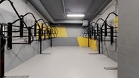 Located at 8446 S Dixie Hwy in Miami, FL, this dedicated bicycle storage facility is a purpose-built, single-level space designed to accommodate a large number of bicycles in an organized and secure environment. The room is outfitted with rows of freestanding black steel bike racks positioned along both sides, maximizing storage capacity while maintaining a clear central aisle for easy access and movement. A standalone bike pump station is available near one end of the room, providing a convenient amenity for cyclists. The interior features a smooth, light-colored concrete floor that is easy to maintain and well-suited to high-traffic use. Overhead, exposed piping and fluorescent lighting fixtures run along the ceiling, providing consistent illumination throughout the space. The walls are finished in a striking geometric mural of bold yellow and varying shades of gray, giving the utilitarian space a modern, energetic aesthetic. The concrete block construction is visible in places, reinforcing the space's durable, functional character. The overall design balances practicality with visual appeal, making this bike storage room a well-equipped and thoughtfully finished facility for residents or building occupants seeking secure, convenient bicycle parking in Miami.