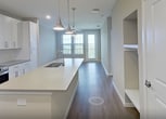 This 690-square-foot, one-bedroom, one-bathroom apartment at 2300 Hooks St, Unit 5211, in Clermont, FL offers a thoughtfully designed open-concept layout with modern finishes throughout. The combined kitchen and living area serves as the heart of the unit, featuring warm wood-look vinyl flooring, recessed lighting, and a ceiling fan. The kitchen is outfitted with crisp white shaker-style cabinetry extending to the ceiling, gray quartz countertops, stainless steel appliances including a refrigerator, range, and built-in microwave, and a large center island with a sink and pendant lighting — ideal for both meal prep and casual dining. A stacked washer and dryer unit is conveniently integrated into the living area. The living room opens to a balcony through a glass door, providing outdoor views and natural light through large windows. The 190-square-foot primary bedroom includes a ceiling fan, two windows with outdoor views, and direct access to a spacious walk-in closet with built-in shelving and dual hanging rods. The bathroom features a white vanity with gray quartz countertop, a framed mirror, and a glass-enclosed shower, all set on wood-look flooring for a clean, cohesive aesthetic.