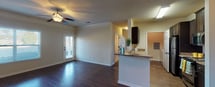 Located at 2000 Broadstone Way in Apex, NC, this single-story residence offers a well-considered layout that balances open communal spaces with defined private areas. The living room serves as the central gathering space, showcasing rich, dark hardwood-style flooring, crown molding, and a ceiling fan with a light fixture. Large windows and a glass-paned exterior door invite abundant natural light while offering outdoor views, creating a bright and welcoming atmosphere.

The kitchen is designed in a galley configuration, featuring dark espresso-toned cabinetry paired with granite-style countertops that extend to a peninsula breakfast bar visible from the living area. Stainless steel and black appliances, including a refrigerator, range, and built-in microwave, complement the cabinetry. Wood-style flooring continues through the kitchen, maintaining a cohesive aesthetic.

The bedroom features neutral carpet flooring and benefits from dual windows positioned on adjacent walls, allowing natural light to fill the space from multiple angles. The textured ceiling is consistent throughout the residence, adding subtle architectural character. Overall, the space presents a practical and comfortable single-floor living environment with consistent finishes throughout.