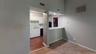 Located at 2700 Cottage Place in Greensboro, North Carolina, this single-floor residence offers a practical and well-organized layout designed for comfortable living. The interior is finished throughout in a neutral gray color palette, complemented by crisp white trim and baseboards, creating a clean and cohesive aesthetic.

The living area is carpeted and generously sized, with a sliding glass door fitted with vertical blinds that allows natural light to filter in and provides a view of the surrounding greenery. The entry door opens directly into this space, which transitions seamlessly into the kitchen via an arched pass-through counter — a functional design detail that enhances connectivity between the rooms.

The kitchen features warm hardwood-style flooring, white cabinetry, speckled laminate countertops, a stainless steel sink, and black appliances including a range and dishwasher, all under recessed lighting. A range hood is mounted above the stove for added ventilation.

The bedroom is carpeted and well-lit, with a window that frames outdoor tree views, providing a calm and natural atmosphere. A standout feature is the built-in vanity area with a wide mirror and white cabinetry with a matching speckled countertop, adding a touch of elegance and practicality. A walk-in closet is also visible, offering ample storage. Textured ceilings are present throughout the unit.