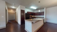 Located at 1201 Albert Ave in Midland, Texas, this single-floor unit offers a thoughtfully designed layout with a cohesive blend of dark wood tones and neutral finishes throughout. The kitchen serves as a central highlight, showcasing rich, dark cabinetry that extends floor to ceiling, granite countertops, and a suite of black appliances including a range, microwave, refrigerator, and dishwasher. A peninsula with a granite surface provides additional prep space and doubles as a casual dining or gathering area. Dark hardwood-style flooring runs through the kitchen and living areas, lending a warm, polished feel. The bedrooms are carpeted and feature ceiling fans, natural light from large windows with blinds, and generous closet space with panel-style doors. The bathrooms are finished consistently with the rest of the unit, featuring dark wood vanities, granite countertops, large mirrors, and tiled tub-shower combinations with hardwood-style flooring. The neutral wall tones throughout create a clean, versatile backdrop. The unit's single-level layout ensures easy accessibility and a seamless flow between living, dining, kitchen, and bedroom spaces.