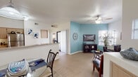 This single-floor residence offers a thoughtfully designed layout that seamlessly connects its key living areas. The open-concept living and dining space is anchored by light wood-look flooring, a ceiling fan with light fixture, and a striking teal accent wall that adds a pop of color to the otherwise neutral palette. Multiple windows dressed with slatted blinds allow generous natural light to fill the space, creating a bright and welcoming ambiance. The living area accommodates comfortable seating and benefits from soaring vaulted ceilings that enhance the sense of openness.

The galley-style kitchen is well-equipped with stainless steel appliances, including a range, microwave, and refrigerator, complemented by light wood cabinetry and an extended granite-style countertop that doubles as a breakfast bar. A pendant light fixture illuminates the adjacent dining area, which features a glass-top table and stylish rug.

The bedroom is a serene retreat with plush carpeting, arched and standard windows that invite natural light, and ample wall space. A generous walk-in closet with built-in shelving and hanging rods provides excellent storage. The full bathroom includes a wide vanity with light wood cabinetry, a large mirror with overhead lighting, and a tiled shower-tub combination.