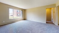 This two-bedroom, one-bathroom unit at Berkshire offers a straightforward, single-floor layout designed for comfortable everyday living. The living room is generously sized, featuring plush wall-to-wall carpeting, a large sliding window that draws in natural light and provides views of the surrounding brick exterior buildings, and baseboard heating along the perimeter walls.

The galley-style kitchen is efficiently arranged, featuring white cabinetry, a double-basin sink, a white refrigerator, and a white range. Wood-look flooring runs through the kitchen, and a wall-mounted air conditioning unit provides climate control. A window above the sink adds natural light to the space.

Both bedrooms are carpeted and well-proportioned, each equipped with a closet offering built-in shelving for organized storage. The rooms are finished with neutral-toned walls and baseboard heating, and windows allow natural light to filter in.

The bathroom features warm-toned ceramic tile lining the tub surround and wainscoting, complemented by a mosaic tile floor in a basketweave pattern. A full bathtub with an overhead shower, toilet, and vanity complete the space, with chrome fixtures providing a clean, polished finish throughout.