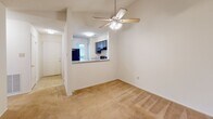 This single-story residence at 1312–1322 Longcreek Drive in Columbia, South Carolina offers a well-organized layout with a cohesive, neutral design aesthetic throughout. The living area is finished with plush wall-to-wall carpeting and features a ceiling fan with integrated lighting. A pass-through counter connects the living space to the kitchen, maintaining an open feel while providing a clear visual distinction between the two areas.

The kitchen is equipped with dark cabinetry, a black Amana electric range with an overhead exhaust hood, and striking granite countertops with a blue-white veining pattern. A black refrigerator and natural light from a nearby window complete the functional workspace.

A bedroom offers sliding glass door access to an outdoor patio or balcony, allowing for natural light and greenery views. A separate room features built-in shelving and a built-in dresser unit, providing practical storage solutions within the space.

The bathroom is well-appointed with the same granite countertop seen in the kitchen, paired with blue-gray cabinetry, a large vanity mirror, pendant lighting, and a generously sized window that brings in natural light. Overall, the space presents a clean, consistent finish with coordinated materials across all rooms.