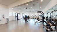 Located at 4739 Starr Ranch Rd in Indian Land, SC, this fitness center is a comprehensive, single-floor facility designed to support a wide range of workout routines. The space is organized into distinct training zones, each outfitted with professional-grade equipment to meet varied fitness needs.

The strength and cardio area features a generous open floor plan with smooth, light-toned flooring and crisp white walls that lend a clean, modern aesthetic. Treadmills and stationary bikes line the perimeter near large windows, flooding the space with natural light and offering views of the surrounding community. Ceiling fans and recessed lighting provide both comfort and visibility throughout. Cable machines, weight benches, free weights, and multi-station strength equipment from brands such as True and Atrus are thoughtfully distributed across the floor.

A dedicated functional training zone showcases TRX suspension systems, battle ropes, medicine balls, and a heavy training tire, all positioned alongside full-length mirrors that enhance spatial awareness during workouts. This section is well-suited for high-intensity interval and cross-training exercises.

A smaller, more intimate training area near the entrance offers additional cable machines and adjustable benches, ideal for personal or small-group sessions. Throughout the facility, tray ceilings add architectural depth, while the open layout ensures ample room to move freely between stations.