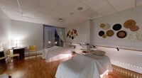 Located at 2500 Edwards Dr in Fort Myers, FL, this single-floor wellness spa offers a thoughtfully designed environment dedicated to relaxation and holistic care. The reception area makes a striking first impression with a bold teal and gold tropical botanical mural, a curved wood-and-granite front desk, light hardwood flooring, and an elegant crystal chandelier overhead — setting a luxurious yet welcoming tone.

Beyond reception, a hallway connects a variety of specialized treatment spaces. A couples massage suite features two treatment tables, warm hardwood floors, woven wall décor, and ambient blue lighting for a calming atmosphere. A multi-station treatment area utilizes white privacy curtains on gold-toned ceiling tracks, with individual treatment beds, accent lighting, and soft neutral tones. A dedicated private treatment room is enveloped in deep navy blue walls with built-in white cabinetry, a granite countertop, a sink, and professional skincare supplies. Another intimate room features rich purple walls, ambient floor lighting, wall sconces, and a treatment bed — ideal for bodywork or energy sessions. A yoga and meditation studio rounds out the space, showcasing hardwood floors, a mirrored wall, ambient LED border lighting, and a star-projection ceiling that creates an immersive, contemplative environment. A bathroom and additional utility areas complete this well-appointed spa.