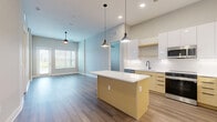 Located in Kissimmee, FL, this well-appointed 2-bedroom, 2-bathroom residence offers a thoughtfully designed single-floor layout with modern finishes throughout. The open-concept living area seamlessly connects the kitchen, dining, and living spaces, creating a bright and airy atmosphere enhanced by recessed lighting and natural light from large windows. The contemporary kitchen is a standout feature, boasting a central island with a clean white countertop, warm wood-toned cabinetry, stainless steel appliances including a refrigerator, microwave, and dishwasher, complemented by sleek pendant lighting overhead. Wood-look flooring runs throughout the home, adding warmth and continuity to every room. The generously sized primary bedroom offers ample space and is served by a dedicated closet, while the second bedroom features a large window with outdoor views of the surrounding landscape. Both bathrooms are finished in a clean, modern style; one features a glass-enclosed shower with tile surround, a floating wood vanity, and a backlit mirror. Additional conveniences include an in-unit laundry room and a utility room. The exterior setting includes landscaped grounds and open surroundings typical of the Kissimmee area.