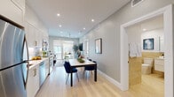 This single-floor residence showcases a thoughtfully designed open-concept layout that seamlessly connects the kitchen, dining, and living areas. Light hardwood flooring runs throughout, creating a cohesive and airy aesthetic. Recessed lighting and ceiling fans contribute to a bright, comfortable atmosphere across the main living spaces.

The kitchen is a standout feature, outfitted with white shaker-style cabinetry accented by brushed gold hardware, a striking marble-look backsplash, white quartz countertops, and a full suite of stainless steel appliances. Under-cabinet lighting enhances both functionality and ambiance. The dining area sits centrally within the open layout, flowing naturally into the living room, which is anchored by floor-to-ceiling sliding glass doors that open to an outdoor space and allow abundant natural light.

The primary bedroom features a bold slate-blue accent wall, ceiling fan, recessed lighting, and wall sconces, creating a calm and stylish retreat. A second bedroom offers a minimalist design with a tall window framing outdoor views. The bathroom is elegantly appointed with full-height travertine-toned tile, a frameless glass shower enclosure, gold fixtures, and a floating white vanity, delivering a refined, spa-like finish.