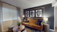 This well-appointed single-floor residence blends contemporary design with warm, inviting touches throughout. The living room serves as the centerpiece of the space, anchored by a rich caramel leather sofa and a striking dark accent wall adorned with a gold-framed triptych of botanical artwork. Wood-look plank flooring, layered textures, and natural light streaming through large windows with linen drapes create a sophisticated yet comfortable atmosphere. A sculptural wood coffee table and curated greenery complete the modern aesthetic.

The kitchen is outfitted with light wood cabinetry, sparkling stone countertops, a stainless steel undermount sink, and stainless steel appliances, including a built-in dishwasher. The clean, minimal design maximizes functionality while maintaining a bright and airy feel.

The space includes two bedrooms, each thoughtfully designed. The primary bedroom features a bold accent wall with gold-framed artwork, a leather-look upholstered headboard, and soft, layered bedding, while a large window fills the room with natural light. The secondary bedroom maintains a calm, neutral palette with warm wood furnishings and sheer curtains.

The bathroom is finished with wood-look tile flooring, a full tub-shower combination, and light wood vanity cabinetry, offering a clean and functional design.