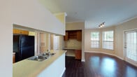 Located at 13100 W Bellfort Ave in Houston, Texas, this single-story residence offers a well-designed, functional layout with a cohesive interior style throughout. The open living and dining area is bathed in natural light from multiple large windows with views of surrounding greenery, and features rich, dark hardwood flooring and crown molding that lend a polished finish to the space. A ceiling fan with light fixture adds comfort and a classic touch.

The kitchen is thoughtfully designed with light stone countertops, a double-basin sink, warm wood cabinetry, black appliances including a range and refrigerator, and an open pass-through that connects seamlessly to the living area. A built-in desk nook with upper shelving and lower cabinetry provides a convenient workspace just off the kitchen.

The hallway leads to the private areas of the residence, where the bathroom features a full tub-shower combination with white tile surround, dark hardwood flooring, and a vanity with matching countertops. The walk-in closet offers generous storage with multiple tiers of wire shelving. A dedicated laundry room houses a full-sized washer and dryer along with additional wire shelving above. The entry area transitions from tile to hardwood flooring, creating a natural delineation of spaces throughout this practical and comfortable Houston home.