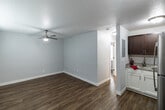 Located at 401 11th St N in Naples, FL, this one-bedroom, one-bathroom unit offers a thoughtfully organized single-floor layout that maximizes every square foot. The open-plan living, dining, and kitchen area serves as the heart of the home, featuring warm wood-look plank flooring and light gray walls that create a clean, cohesive aesthetic. The kitchen is equipped with rich dark-wood upper cabinetry, white lower cabinetry, a granite-style countertop with an undermount sink, and stainless steel appliances, including a full-size refrigerator. A ceiling fan with a light fixture in the living area and a window with white blinds allow for natural light and air circulation, while a wall-mounted AC unit ensures climate comfort. The bedroom continues the same wood-look flooring and neutral palette, fitted with a ceiling fan and a window with blinds that brings in additional natural light. A dedicated closet provides practical storage. The bathroom features full white subway tile surround encasing a soaking tub with a showerhead, complemented by brushed gold fixtures and a frosted privacy window. A hallway connects the main living space to the private quarters, keeping the layout functional and well-defined.