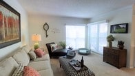 Located at 1900 N US-17 Hwy in Mount Pleasant, South Carolina, this single-floor residence offers a welcoming and well-appointed living environment. The living area is a standout feature, bathed in abundant natural light streaming through large windows fitted with horizontal blinds, which also provide views of the outdoor surroundings. The space is finished with neutral-toned carpeting that adds warmth underfoot and complements the light-colored walls throughout. The living room provides generous room for comfortable furnishings, including a sectional sofa, a chaise lounge, and a central ottoman that doubles as a coffee table — creating a versatile and functional gathering space. Decorative touches such as wall art and a classic clock lend a personalized, homey character to the interior. The textured ceiling adds subtle architectural detail, while the overall layout promotes an open and airy ambiance. Positioned along US-17 in Mount Pleasant, this residence benefits from convenient access to the shopping, dining, and recreational offerings that characterize this vibrant South Carolina community, while maintaining a quiet and comfortable interior retreat.