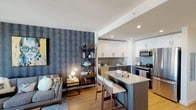 This contemporary 2-bedroom, 2-bathroom residence at 45 Main St in Yonkers, NY offers a thoughtfully designed open-concept layout with modern finishes throughout. The living and dining area is bright and inviting, featuring warm hardwood flooring, floor-to-ceiling windows that frame sweeping views of the city skyline and the Hudson River beyond, and a bold textured accent wall that adds visual depth and character.

The kitchen is well-appointed with sleek two-tone cabinetry — white uppers paired with dark lower units — stainless steel appliances including a gas range, microwave, and dishwasher, and a generous center island with bar seating, ideal for casual dining or entertaining.

Both bedrooms are generously sized with large windows that capture expansive elevated views of the surrounding cityscape and river. The primary bedroom benefits from a corner window configuration, maximizing natural light and panoramic sightlines.

The two bathrooms are finished with striking dark herringbone-pattern tile flooring. One bathroom features a soaking tub with shower, while the other is equipped with a frameless glass walk-in shower, both paired with modern wood-toned vanities and clean white walls that create a sleek, spa-like aesthetic. The unit's elevated position enhances the sense of openness and light throughout every room.