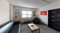 Located at 635 Contanche St in Greenville, NC, this single-floor unit offers a practical and functional layout well-suited for student living. The living area serves as the central gathering space, featuring carpeted flooring, a textured ceiling, a ceiling fan, and a wall-mounted HVAC unit. Large windows with blinds allow natural light to fill the room, creating a comfortable atmosphere for relaxing or socializing.

The kitchen runs along one wall and is equipped with white cabinetry, a gas range, a built-in microwave, and a sink with countertop workspace. Warm-toned hardwood-style flooring adds a welcoming feel to this area, which also provides direct access to the unit's entry door.

The unit includes multiple bedrooms, each carpeted and finished with textured ceilings. One bedroom features a ceiling fan with built-in lighting and closet access, while another includes a desk and chair alongside a window overlooking the surrounding building exterior. Each bedroom offers a quiet, personal space suited for rest and study.

The bathroom is clean and efficiently designed, featuring a vanity with mirror, toilet, and a shower enclosed by a curtain. Overall, this unit provides a straightforward, functional living environment with all essential amenities in a compact, well-organized single-floor layout.