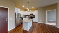 Located at 1606 Prairie Pl in Holmen, Wisconsin, this single-floor residence offers a well-organized layout with a clean, contemporary aesthetic throughout. The open living area is anchored by rich, dark hardwood flooring and features a ceiling fan with light fixture, creating a comfortable and inviting atmosphere. Natural light flows in through large windows, and a glass door provides convenient access to the exterior.

The kitchen is a standout feature, showcasing crisp white cabinetry, dark countertops, a granite-topped center island with pendant lighting, stainless steel appliances including a refrigerator and range, and recessed ceiling lights. The space is both functional and stylish, ideal for everyday cooking and entertaining.

The bedrooms are carpeted for warmth and comfort, each receiving natural light through windows fitted with blinds. The layout includes two bathrooms: one full bath with a tub-shower combination, tile flooring, and a single vanity, and a second bathroom with similar finishes and an extended layout offering additional utility space.

A dedicated utility area with laundry hookups is accessible from within the home. Throughout, neutral taupe wall tones and white trim provide a cohesive, move-in-ready feel that complements the home's practical and comfortable design.