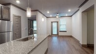 This single-floor residence showcases a thoughtfully designed open-concept layout connecting the kitchen and living areas. The kitchen serves as a central highlight, featuring dark espresso cabinetry extending to the ceiling, granite countertop surfaces, and a large island with an undermount sink and pendant lighting overhead. Stainless steel appliances, including a range, over-the-range microwave, dishwasher, and refrigerator, complete the well-appointed cooking space.

The living area flows seamlessly from the kitchen, bathed in natural light from multiple windows fitted with horizontal blinds. A ceiling fan with integrated lighting provides comfort and ambiance, while recessed lighting and crown molding add refined architectural detail throughout. Wood-look plank flooring runs consistently across all rooms, contributing to a cohesive, contemporary aesthetic.

The bathroom features a dual-sink vanity with matching granite countertops, dark cabinetry, and a large framed mirror illuminated by overhead lighting. An additional bedroom offers natural light through a pair of windows and ample open floor space. Interior doors throughout maintain a consistent paneled gray finish, tying the design together with a clean, modern sensibility.