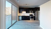 Located at 20 W Northwest Highway in Mount Prospect, Illinois, this single-floor residence offers a thoughtfully designed layout with modern finishes throughout. The open-concept living and kitchen area serves as the heart of the space, featuring wide-plank hardwood-style flooring, neutral gray walls, and track lighting that creates a clean, contemporary ambiance. Large sliding glass doors flood the area with natural light and provide direct access to an outdoor patio, offering views of the surrounding exterior.

The kitchen is a standout feature, outfitted with bold dark cabinetry that extends from floor to ceiling, contrasting elegantly with light countertops and a classic white subway tile backsplash. A full suite of stainless steel appliances — including a refrigerator, electric range, over-the-range microwave, and dishwasher — completes the functional and stylish cooking space.

The living area is open and versatile, with ample room for flexible furniture arrangements and a window that draws in additional natural light. The bathroom is well-appointed with a full tub and tiled surround, a dark-framed vanity mirror, white undermount sink, and wood-look flooring that ties the space together with a cohesive, modern aesthetic throughout.