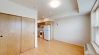 This efficient single-floor unit is thoughtfully laid out to maximize every square foot, comprising a living room, kitchen, bathroom, and two closets. Light hardwood flooring runs throughout, lending warmth and visual continuity across all spaces.

The living room is bright and open, anchored by a pair of large windows fitted with blinds that frame views of the surrounding neighborhood. A wall-mounted HVAC unit provides climate control, and the clean white walls create a neutral, welcoming ambiance.

The kitchen is well-appointed with warm honey-toned wood cabinetry extending from floor to ceiling, offering generous storage. A stainless steel sink, white electric range with coil burners, and a full-size refrigerator complete the functional setup, all set against crisp white countertops.

The bathroom is clean and simply finished, featuring a wood-toned vanity with an integrated sink, a wall mirror, and a combined tub and shower. Consistent light wood flooring ties the space to the rest of the unit.

Two closets provide practical storage solutions, including one with a distinctive natural wood-panel door. Recessed and flush-mount ceiling lighting throughout keeps the unit well-illuminated. The overall design is clean and functional, with a consistent palette of light wood and white tones.