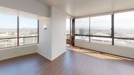 This single-floor residence showcases a thoughtfully designed open layout with distinct living areas finished to a high modern standard. The main living area features warm hardwood flooring and expansive floor-to-ceiling windows that flood the space with natural light while framing impressive panoramic views of the cityscape and surrounding mountains. A dedicated outdoor access point further connects the interior to these sweeping vistas.

The kitchen is well-appointed with marble-style quartz countertops, light wood cabinetry, white subway tile backsplash, and a full suite of stainless steel appliances including a refrigerator, range, microwave, and dishwasher. Recessed lighting enhances the clean, functional workspace.

The bedrooms are carpeted for comfort and feature clean white walls and ample natural light. One bedroom includes a built-in closet with frosted glass sliding doors and integrated shelving, providing organized storage.

The bathroom offers a refined aesthetic with a long dual-sink vanity set in light wood cabinetry, a large mirrored medicine cabinet, and a marble-tiled shower surround. Hardwood flooring continues into this space, tying the design together cohesively throughout.