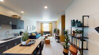 This single-story studio in Mesa, Arizona, offers a thoughtfully designed open-concept layout that maximizes every square foot. Light wood-style flooring flows continuously throughout the space, creating a cohesive and airy feel. The living area is anchored by a bold mustard-yellow accent wall, which adds warmth and visual interest against the neutral white walls. Recessed lighting illuminates the space, while a window dressed with golden curtains allows natural light to filter in.

The kitchen is a standout feature, outfitted with dark espresso cabinetry that extends to the ceiling, providing ample storage. Stainless steel appliances — including a refrigerator, electric range, over-the-range microwave, and dishwasher — complement crisp white countertops. A butcher-block dining table positioned nearby serves as both a workspace and dining area.

The open floor plan seamlessly integrates the living and sleeping zones, offering flexibility in how the space is arranged. The bathroom is clean and functional, featuring a full tub-shower combination, a white vanity with an undermount sink, and a round mirror. The overall ambiance is modern and inviting, blending contemporary finishes with warm tones.
