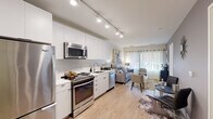 Located in Washington, DC's vibrant NoMa/Trinidad neighborhood, this single-floor residence offers a thoughtfully designed open-concept layout. The kitchen is a standout feature, outfitted with sleek white cabinetry extending to the ceiling, white quartz countertops, and a full suite of stainless steel appliances including a Whirlpool refrigerator, electric range, over-the-range microwave, and dishwasher. Track lighting overhead ensures excellent task illumination throughout the cooking space. The kitchen flows seamlessly into the living area, which is bathed in natural light from large sliding glass doors and draped windows. Light hardwood flooring runs continuously throughout the main living spaces, enhancing the sense of openness. The space includes multiple bedrooms, each featuring natural light from curtained windows. One bedroom offers closet access and versatile flexible-use potential. The bathroom is clean and modern, featuring a tiled floor, a tub-shower combination with white tile surround, and a contemporary vanity. The overall aesthetic is modern and neutral, with crisp white walls and consistent finishes that create a bright, cohesive living environment well-suited for urban DC living.