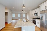 Located at 98 Old Gonic Rd. in Rochester, NH, this well-appointed three-story home offers four bedrooms and four bathrooms across a thoughtfully designed layout. The ground floor features an attached garage with an automatic opener, providing convenient interior access.

The main living level showcases an open-concept design where the kitchen flows seamlessly into the living room. The kitchen is a standout feature, centered around a large island with a striking granite countertop, undermount sink, and pendant lighting. White shaker-style cabinetry, stainless steel appliances including a gas range, microwave, and refrigerator, complete the space. Light hardwood flooring and recessed lighting extend throughout, and a sliding glass door opens to an outdoor deck area.

The hallway leading to the kitchen features clean-lined shaker-style interior doors with matte black hardware, lending a contemporary touch. The bathrooms are finished with marble-look tile flooring, granite vanity tops, and subway tile tub surrounds.

The upper floor houses the bedrooms, including a generously sized primary bedroom with recessed lighting and natural light from multiple windows. Additional bedrooms offer warm hardwood floors, natural light, and closet storage. The home presents a clean, modern aesthetic throughout with neutral tones, crisp white trim, and quality finishes at every turn.