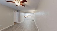 This single-floor unit offers a bright and functional layout designed for comfortable everyday living. The open living area is finished with light-toned wood-look flooring and neutral gray walls, creating a clean and versatile backdrop. A ceiling fan with a built-in light fixture provides both airflow and ambient lighting, while wall-mounted sconces add a warm accent. A window with blinds allows natural light to fill the front of the space, and a wall-unit HVAC system ensures year-round climate control. The kitchen is efficiently arranged with ample white cabinetry extending to the ceiling, stone-toned countertops, and a skylight panel overhead that brightens the workspace. White appliances, including a range, over-the-range microwave, and refrigerator, are included. The bedrooms feature plush carpeting, ceiling fans, and windows that invite natural light, offering a comfortable and restful atmosphere. A closet provides convenient storage within the bedroom area. The bathroom is neatly appointed with a white vanity, solid surface countertop, large mirror, multi-bulb vanity lighting, and wood-look flooring that ties the space together cohesively. Throughout the unit, clean finishes and a consistent neutral palette contribute to a move-in-ready, well-maintained ambiance.