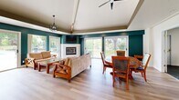 Located at 1175 Lake Blvd in Davis, CA, this single-floor community space offers a thoughtfully designed layout that balances social gathering and active living. The heart of the space is a bright, open-plan kitchen and dining area finished with light hardwood flooring throughout. The kitchen features white cabinetry, stone countertops, stainless steel appliances, and a striking teal curved island with bar seating, illuminated by modern pendant lights. Adjacent to the kitchen, the dining and lounge area is defined by bold teal accent walls, a vaulted ceiling with decorative beam detailing, a tiled fireplace, and large sliding glass doors that invite abundant natural light and provide views of the surrounding greenery. A ceiling fan and ample seating make this space ideal for gatherings of all sizes. The dedicated exercise room is well-lit with both natural and overhead fluorescent lighting, outfitted with multiple cardio machines including treadmills, ellipticals, and stationary bikes, and features durable tile flooring with mirrored wall accents. Two ADA-accessible bathrooms, finished with warm wood-toned vanities, light green walls, and hardwood-style flooring, provide convenient and inclusive facilities. A connecting hallway ties all areas together seamlessly.