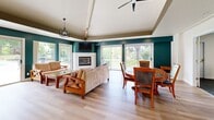 Located at 1175 Lake Blvd in Davis, CA, this single-floor community space offers a thoughtfully designed layout that balances social gathering and active living. The heart of the space is a bright, open-plan kitchen and dining area finished with light hardwood flooring throughout. The kitchen features white cabinetry, stone countertops, stainless steel appliances, and a striking teal curved island with bar seating, illuminated by modern pendant lights. Adjacent to the kitchen, the dining and lounge area is defined by bold teal accent walls, a vaulted ceiling with decorative beam detailing, a tiled fireplace, and large sliding glass doors that invite abundant natural light and provide views of the surrounding greenery. A ceiling fan and ample seating make this space ideal for gatherings of all sizes. The dedicated exercise room is well-lit with both natural and overhead fluorescent lighting, outfitted with multiple cardio machines including treadmills, ellipticals, and stationary bikes, and features durable tile flooring with mirrored wall accents. Two ADA-accessible bathrooms, finished with warm wood-toned vanities, light green walls, and hardwood-style flooring, provide convenient and inclusive facilities. A connecting hallway ties all areas together seamlessly.