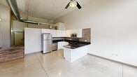 Located at 1900 E Superior Ave in Cleveland's vibrant near-east side, this loft-style unit blends industrial character with modern finishes across a single open floor. The space is immediately distinguished by its soaring ceilings, exposed ductwork, and original brick walls, all hallmarks of its historic building conversion. Large arched windows flood the interior with natural light while offering views of the surrounding neighborhood.

The kitchen is a standout feature, designed with a clean, contemporary aesthetic. White shaker-style cabinetry reaches toward the tall ceilings, complemented by dark granite countertops and a mosaic tile backsplash in warm earth tones. Stainless steel appliances — including a full-size refrigerator, range, microwave, and dishwasher — complete the functional and stylish cooking space. A peninsula provides additional counter space and casual dining potential. Track lighting and a ceiling fan overhead add both practicality and character.

The open main living area features large-format tile flooring, creating a seamless and easy-to-maintain surface throughout. Exposed HVAC ductwork running along the ceiling reinforces the industrial loft aesthetic.

The bathroom is neatly appointed with a tub-shower combination, accented by a mosaic tile border that ties back to the kitchen's design palette, offering a cohesive look throughout the unit.