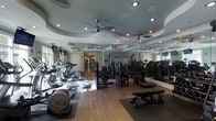 This fitness center offers a comprehensive workout environment designed to accommodate a variety of exercise routines. The space is anchored by gleaming hardwood flooring and features an eye-catching tiered ceiling with sculpted, layered molding painted in soft tones, adding an unexpected elegance to the room. Multiple ceiling fans are evenly distributed throughout, ensuring consistent air circulation during workouts.

The cardio section is well-stocked with a lineup of treadmills, elliptical trainers, and step machines, all positioned to take advantage of the natural light filtering in through the windows. The strength training area offers a robust selection of cable machines, resistance equipment, and adjustable benches, catering to both beginners and experienced fitness enthusiasts.

Full-length mirrors line one wall, amplifying the sense of space and allowing users to monitor their form during exercise. Recessed lighting is thoughtfully integrated into the ceiling alongside the fans, providing bright, even illumination throughout. The overall ambiance is polished and welcoming, blending functional fitness equipment with refined architectural details to create a space that feels both motivating and comfortable.