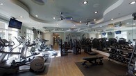 This fitness center offers a comprehensive workout environment designed to accommodate a variety of exercise routines. The space is anchored by gleaming hardwood flooring and features an eye-catching tiered ceiling with sculpted, layered molding painted in soft tones, adding an unexpected elegance to the room. Multiple ceiling fans are evenly distributed throughout, ensuring consistent air circulation during workouts.

The cardio section is well-stocked with a lineup of treadmills, elliptical trainers, and step machines, all positioned to take advantage of the natural light filtering in through the windows. The strength training area offers a robust selection of cable machines, resistance equipment, and adjustable benches, catering to both beginners and experienced fitness enthusiasts.

Full-length mirrors line one wall, amplifying the sense of space and allowing users to monitor their form during exercise. Recessed lighting is thoughtfully integrated into the ceiling alongside the fans, providing bright, even illumination throughout. The overall ambiance is polished and welcoming, blending functional fitness equipment with refined architectural details to create a space that feels both motivating and comfortable.