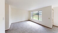 This single-floor, two-bedroom, one-bathroom unit in SeaTac, WA offers a practical and well-organized layout. The combined kitchen and living area forms the heart of the unit. The kitchen features a galley-style design lined with warm wood cabinetry on both sides, offering generous storage, a double-basin stainless steel sink, electric range, and a black refrigerator. A pass-through counter with overhead cabinetry connects the kitchen to the living area, creating an open feel between the two spaces.

The living room is bright and spacious, with large windows and a sliding glass door that fills the room with natural light and provides views of the surrounding greenery. A ceiling fan adds comfort to the area, which features neutral carpet and clean white walls throughout.

Both bedrooms are carpeted and well-lit with windows overlooking outdoor greenery. The primary bedroom offers a notably generous footprint, while the second bedroom provides a comfortable, functional space. Each bedroom includes sliding closet doors with built-in hanging rods for storage.

The bathroom is clean and straightforward, featuring a full-size tub and shower combination with white surround, chrome fixtures, and wood-look flooring. Two hallways connect the rooms, contributing to a logical and easy-to-navigate floor plan.