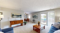 Located at 9115 Knights Bridge Blvd in Indianapolis, Indiana, this 2-bedroom, 2-bathroom single-floor home offers a practical and comfortable layout ideal for everyday living. The open living and dining area is carpeted throughout and filled with natural light, featuring a sliding glass door that leads to an outdoor space with views of a community pool. A ceiling fan overhead and neutral gray walls give the combined area a relaxed, inviting atmosphere. The kitchen features wood-look flooring, ample white cabinetry with wood trim, a built-in pantry with louvered doors, and a full appliance suite including a range and over-the-range microwave. The adjacent dining room benefits from a ceiling fan, a window with blinds, and easy access to the kitchen. The primary bedroom is a well-proportioned retreat with gray walls, plush carpeting, and direct access to both a dedicated closet and a private bathroom. The second bedroom features bold blue walls, a large window with sheer curtains, and generous floor space. Both bathrooms include a shower-tub combination and tile flooring. Additional features include multiple closets throughout, in-unit laundry, and textured ceilings across the home.
