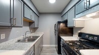 Located at 3058 Allegheny Ave in Columbus, Ohio, this single-floor unit offers a thoughtfully updated interior with a cohesive cool-gray color palette throughout. The entryway opens into a bright living area finished with light wood-look flooring, large windows that invite generous natural light, and a wall-mounted HVAC unit. The space flows into a spacious main living area featuring dark hardwood-style flooring, multiple windows with blinds, and clean white trim that complements the gray walls.

The galley-style kitchen is efficiently designed with gray shaker cabinets, light granite-style countertops, a stainless steel double sink, and black appliances including a gas range and refrigerator. Light tile-style flooring and under-cabinet ventilation complete the kitchen's functional and modern aesthetic.

The bedroom is a quiet, carpeted retreat with soft gray walls, a ceiling fan, and ample room. The bathroom features wood-look flooring, a warm-toned wood vanity with a mirrored medicine cabinet, a toilet, and a bathtub with shower, all set against soft blue-gray walls. Clean lines and updated finishes throughout give this unit a move-in-ready feel with practical, contemporary design.