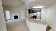 This single-floor residence offers a thoughtfully designed layout that balances open communal spaces with comfortable private areas. The living room serves as the heart of the home, highlighted by soaring vaulted ceilings, soft neutral-toned carpet, and a classic white-mantled fireplace that anchors the room. An open pass-through connects the living area to the kitchen, enhancing the sense of openness and flow throughout.

The kitchen is well-appointed with dark espresso-toned cabinetry, light granite-style countertops, and a full suite of stainless steel appliances including a refrigerator, range, and over-the-range microwave. Light wood-style flooring adds warmth underfoot, and a ceiling-mounted light fixture provides ample illumination. A peninsula with a double sink extends into the space, offering additional prep area and casual dining potential.

The bedrooms are generously sized, each featuring plush carpeting, ceiling fans with light fixtures, and windows fitted with blinds that allow natural light to filter in. The rooms offer a calm, neutral palette well-suited for a variety of uses.

Two bathrooms serve the residence. One features a tub-shower combination with white tile surround and dark upper cabinetry, while the other includes an extended vanity with a large mirror, dark cabinetry, granite-style countertops, and dark hardwood-style flooring, creating a clean and functional space.