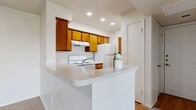 This single-floor residence offers a functional and efficiently organized layout across three bedrooms and two full bathrooms. The open-concept kitchen serves as a central hub of the home, featuring warm honey-toned wood cabinetry, light speckled countertops, and a peninsula with a double stainless steel sink that overlooks the adjacent living area. White appliances, including a coil-burner electric range and a refrigerator, are neatly integrated beneath upper cabinetry with a range hood. Recessed lighting illuminates the kitchen and living spaces effectively.

The living room is carpeted and spacious enough for comfortable furnishing, highlighted by a large sliding glass door fitted with vertical blinds that allows natural light to filter in. A hallway connects the bedrooms, providing a sense of privacy from the main living areas. The primary bedroom is a well-proportioned room with a ceiling fan and natural light from a window. The additional bedrooms are also carpeted and feature windows with blinds. Two closets provide dedicated storage throughout the unit. The bathrooms are finished with wood-toned vanities, light countertops, and tub-shower combinations with white tile surrounds, complemented by wood-look vinyl flooring.