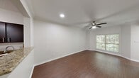 This one-bedroom, one-bathroom unit is located at 7700 N Capital of Texas Hwy in Austin, TX, offering a well-appointed and efficiently designed single-floor layout. Dark hardwood flooring flows throughout the main living areas, complemented by crisp white walls, crown molding, and ceiling fans in both the living room and bedroom. The living room is bright and open, with a large window framing lush, tree-lined views and a recessed light adding to the warm ambiance. The kitchen features dark espresso cabinetry, granite countertops, stainless steel appliances including a refrigerator and dishwasher, and a dark hardwood floor that ties seamlessly into the rest of the living space. The bedroom offers plush carpeting, a ceiling fan, a sizable window with natural views of surrounding greenery, and direct access to the bathroom. The bathroom is well-finished with a granite-topped vanity, dark espresso cabinetry, a large mirror with vanity lighting, and tile flooring. A dedicated closet and two hallways round out the layout, providing practical storage and circulation. The unit also includes a dedicated entry door, adding a sense of privacy and accessibility throughout.