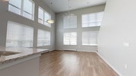 Located at 200 College St in New Haven, CT, this two-floor residence is defined by its striking double-height ceilings and an abundance of natural light. The main living area is expansive and open, with walls of large windows that flood the space with daylight, light wood-style flooring, and a ceiling fan that complements the dramatic vertical scale of the room. The open-concept kitchen flows seamlessly from the living area and is outfitted with dark espresso cabinetry, granite-style countertops, stainless steel appliances including a gas range, microwave, and refrigerator, and a peninsula that provides additional workspace and casual seating. A dedicated nook within the kitchen offers extra storage or a cozy workspace. The upper level features soft carpeting and includes generous closet space with double-door storage, creating comfortable and practical sleeping quarters. A windowed bedroom on this level offers a quiet, well-lit retreat. The bathroom is finished with large-format white tile flooring, a dark vanity with a white countertop, and a full soaking tub. Additional features include a tucked-away storage space under the staircase, adding practical utility to this well-appointed, light-filled New Haven residence.
