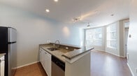 This three-story residence on S Harbor Pl in Portland, Oregon, is thoughtfully laid out across multiple levels connected by an interior staircase. The entry level features a tiled foyer with recessed lighting, a built-in mail shelf, and access to an attached private garage with an automatic opener—a practical convenience in the Pacific Northwest.

The main living level showcases warm wood-style flooring throughout an open-concept layout. The kitchen is equipped with granite countertops, white cabinetry, stainless steel appliances including a range and dishwasher, and a peninsula with a sink that opens directly to the living area. A ceiling fan and large windows allow natural light to fill the space, creating a bright and airy atmosphere.

Upper levels feature carpeted bedrooms with ceiling fans and generous window arrangements that invite natural light. The bathroom includes a wide vanity with a dark countertop and ample mirror space. A dedicated laundry area houses a full-sized washer and dryer with overhead wire shelving for additional storage. The neutral color palette and clean finishes give the home a consistent, move-in-ready aesthetic throughout all three floors.