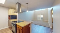 Located at 2002 E Fort Lowell Rd in Tucson, Arizona, this single-floor residence offers a thoughtfully designed layout that balances open communal spaces with comfortable private rooms. The living area immediately impresses with its dramatically high ceilings and a large sliding glass door fitted with vertical blinds, allowing ample natural light to pour in through clerestory windows positioned near the top of the wall. The flooring transitions seamlessly from light wood-style planks in the kitchen and entry areas to plush carpet throughout the living and bedroom spaces. The kitchen is a standout feature, equipped with a central island topped with granite-style countertops, a sleek stainless steel range hood, an electric cooktop, and a black refrigerator. Rich warm-toned cabinetry pairs with light upper cabinets, and pendant lighting adds a polished touch. A pass-through counter opens directly to the living area, reinforcing the open-concept feel. The bedrooms are generously sized, each featuring carpet flooring, ceiling fans with integrated lighting, and windows with blinds that invite natural light. At least one bedroom includes a dedicated closet with a hanging rod. Throughout the residence, neutral tones, clean lines, and practical finishes create a bright, move-in-ready atmosphere well-suited to Tucson's sunny climate.