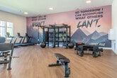 Located at 2015 E Springs Dr in Madison, WI, this fitness center offers a comprehensive and thoughtfully designed exercise space across a single expansive floor. The room is finished with warm hardwood-style flooring and crisp white walls, creating a clean, modern aesthetic that feels both energizing and inviting.

Large windows line one side of the space, flooding the interior with abundant natural light and offering views of the surrounding neighborhood — a welcome backdrop for cardio workouts. Multiple treadmills and elliptical machines are positioned along the window wall to take full advantage of the outdoor views, while stationary bikes and rowing machines occupy additional areas of the floor.

A dedicated strength training zone features a multi-use power rack fully stocked with resistance bands, medicine balls, and a variety of accessories. Free weights, benches, and functional training equipment — including a tire flip trainer — round out the offering, supporting a wide range of workout styles. Recessed lighting throughout the ceiling supplements the natural light during all hours.

Defining the space visually are bold, large-scale motivational murals featuring mountain imagery and inspiring quotes, lending the gym an energetic and motivating atmosphere. The open, uncluttered layout ensures ample room to move freely between equipment, making this fitness center a well-appointed destination for residents pursuing their health and wellness goals.