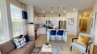 This single-floor residence offers a well-designed open-concept layout where the kitchen, dining, and living areas flow seamlessly together. The kitchen is a standout feature, equipped with stainless steel appliances, crisp white cabinetry, granite countertops, and a subway tile backsplash. A central island with pendant lighting overhead provides additional prep space and casual seating with stylish blue velvet barstools on gold-toned bases. Light wood-style flooring extends throughout the main living areas, contributing to an airy, cohesive feel.

The living area benefits from abundant natural light through large windows and glass doors that open to an outdoor balcony, offering views of surrounding greenery. Ceiling fans are present throughout the residence for added comfort.

The two bedrooms are carpeted for warmth and comfort. One bedroom features a bold teal accent wall, while the other is finished in soft neutral tones, both receiving ample natural light. Each bedroom includes a ceiling fan and dedicated closet space with built-in wire shelving.

The bathroom is well-appointed with granite countertops, white cabinetry, a combination tub and shower, and wood-style flooring, maintaining the consistent, polished aesthetic found throughout the residence.