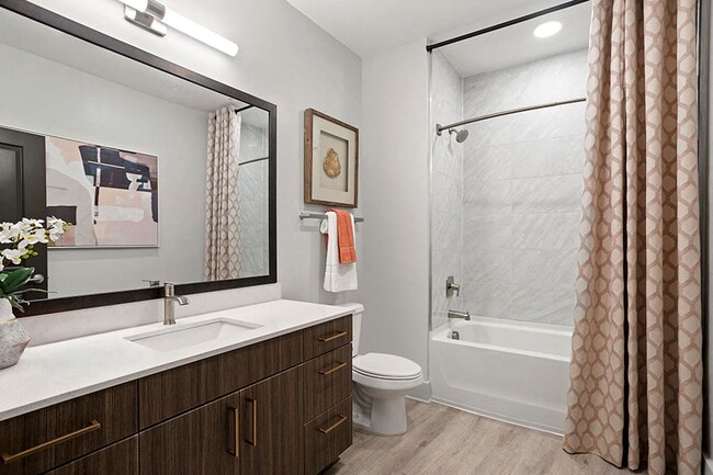 Modern bathrooms with framed mirrors, curved shower rods and quartz countertops - Auden Apartments