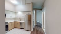 Located at 152 Temple St in the heart of New Haven, CT, this single-floor unit offers a well-designed layout with a cohesive, contemporary aesthetic. The kitchen is a standout feature, equipped with stainless steel appliances including a full-size refrigerator, dishwasher, and gas range. Crisp white upper cabinetry is paired with warm wood-toned lower cabinets, complemented by light countertops and classic white tile flooring, creating a clean and functional cooking space. A hallway connects the kitchen to the rest of the unit, where durable hardwood-style flooring flows through the living and bedroom areas, adding warmth and continuity. The living space is open and versatile, featuring neutral taupe walls, white baseboards, and a textured ceiling. Windows fitted with blinds allow for natural light while maintaining privacy. The bedroom is generously proportioned, with the same hardwood-style flooring and dual windows that bring in additional daylight. The bathroom is neatly appointed with a wood-toned vanity, white countertop, a wall-mounted mirror with a multi-light bar fixture, a tub-shower combination, and white tile flooring. Overall, the unit presents a clean, move-in ready space with modern finishes throughout.